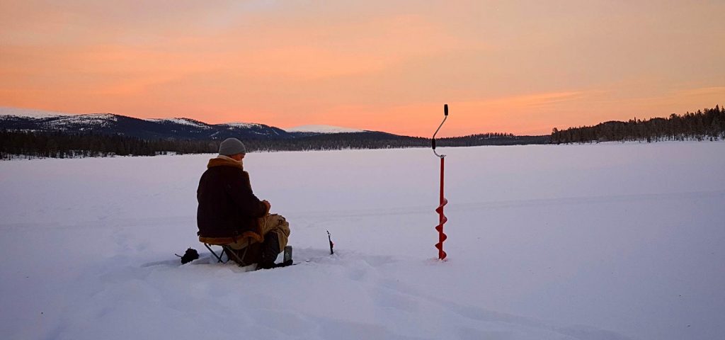 Ein Mann sitzt auf einem zugefrorenen See und betreibt Eisfischen