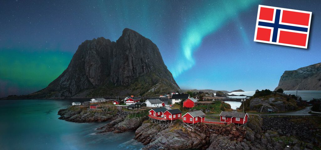 Das Nordlicht über einem Berg und einem Dorf am Wasser in Norwegen